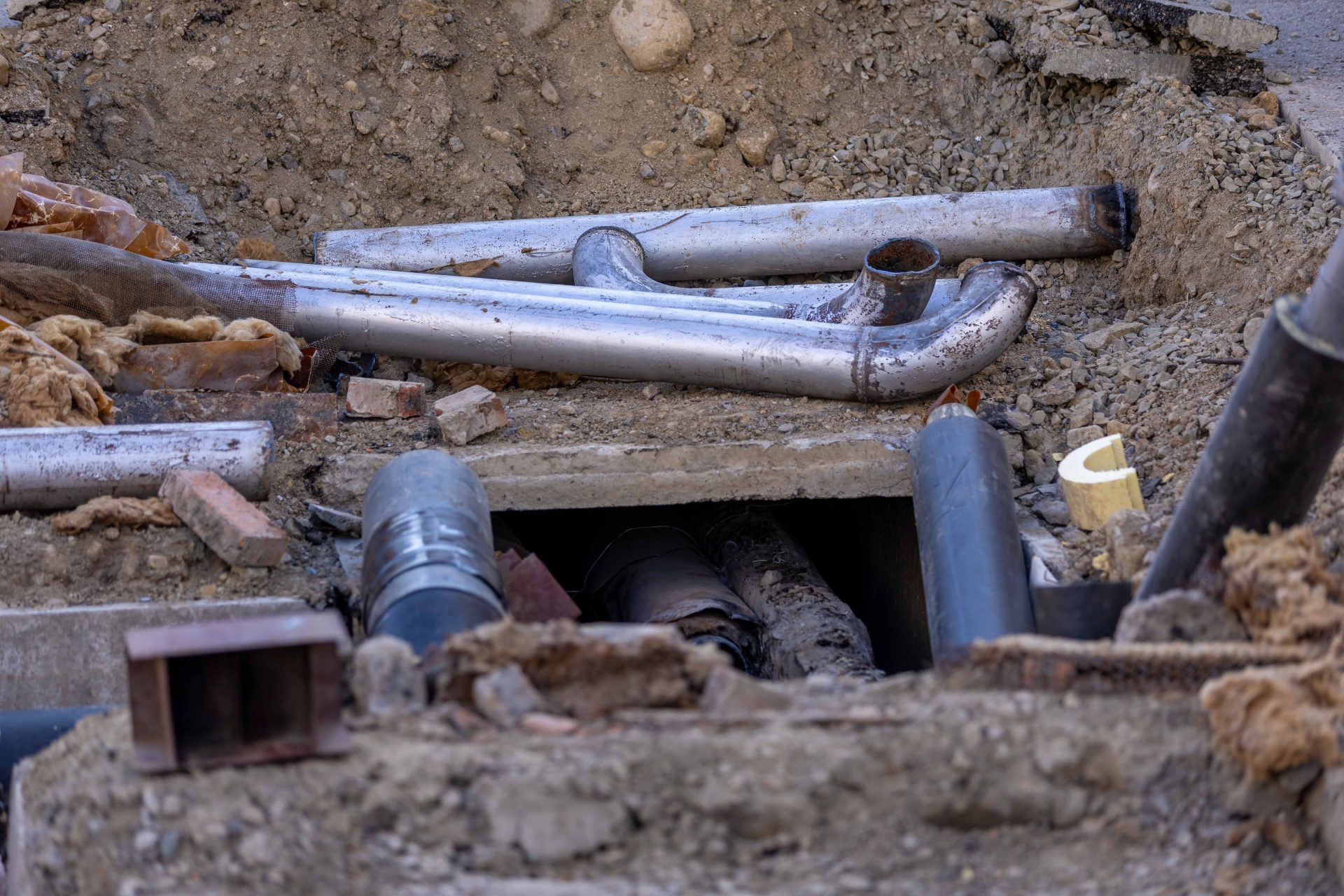 Nahaufnahme einer städtischen Rohrinstallation auf einer Baustelle, die verschiedene Rohre und Materialien zeigt.