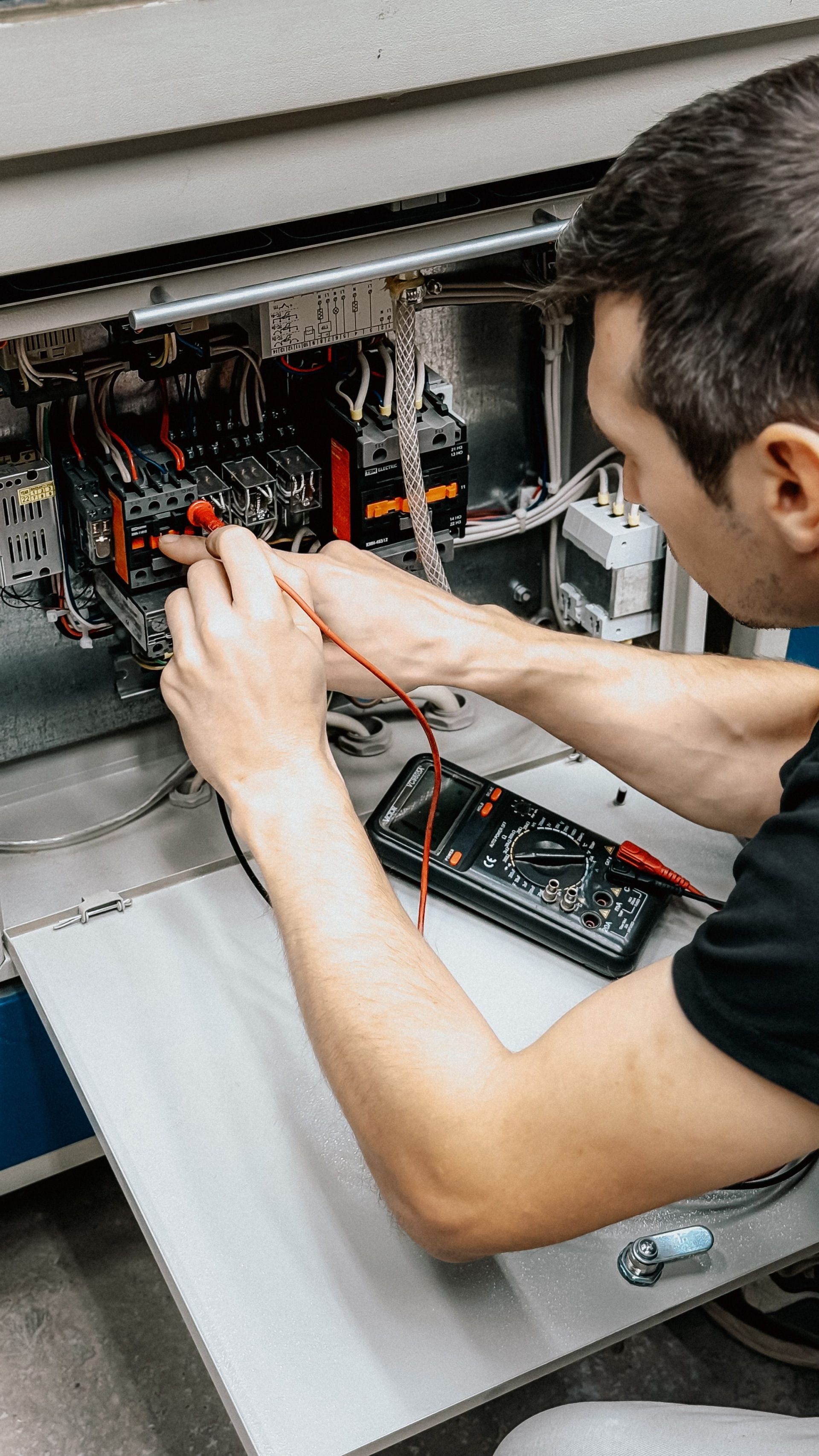 Ein Elektriker verwendet ein Multimeter, um Anschlüsse in einem geöffneten Schaltkasten zu prüfen und zu diagnostizieren.